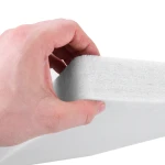 Dłoń trzymająca krawędź białego poliestrowego panelu akustycznego PET 50x100cm, co wyraźnie obrazuje jego 5-centymetrową grubość i chłonną strukturę.