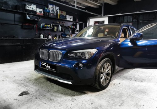 Granatowe BMW X1 zaparkowane w warsztacie, przygotowane do wygłuszania drzwi i maski materiałami Bitmat