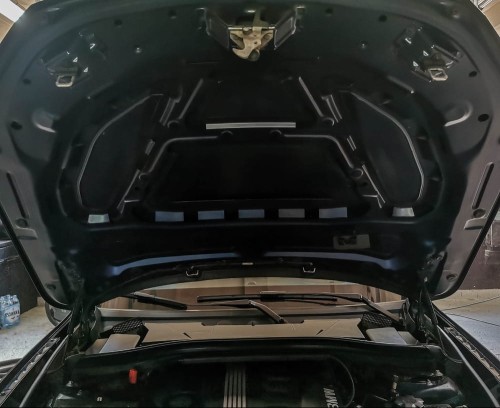 Odsłonięta, wewnętrzna strona maski silnika w BMW X1 w trakcie przygotowań do nałożenia wygłuszenia