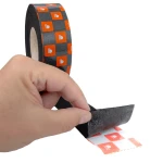 Dłoń odklejająca warstwę zabezpieczającą z logo Bitmat od czarnej, samoprzylepnej taśmy włókninowej.