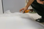 Instalator nanosi klej w sprayu na krawędź białej chmury akustycznej na stanowisku roboczym.